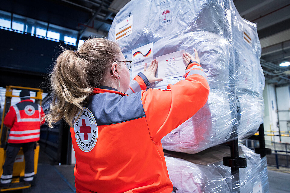 Eine Frau in Einsatzkleidung des Roten Kreuz hilft bei der Verladung von Hilfsgütern des Roten Kreuzes für ein Katastrophengebiet.
