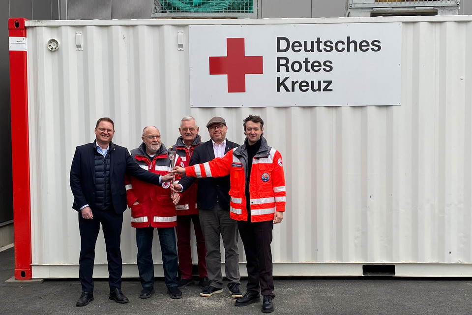 Fünf Männer, davon drei in Einsatzjacken des Roten Kreuz, stehen nebeneinander und halten gemeinsam eine Ölfackel in der Mitte.