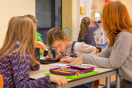 Eine Frau hilft einem Mädchen an einem Schreibtisch in einem Klassenzimmer