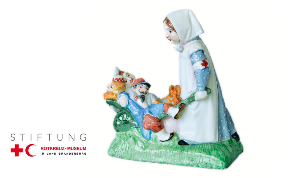 antike Porzellanfigur einer Rotkreuzschwester, die drei verwundete Soldaten in einer Karre vor sich herschiebt