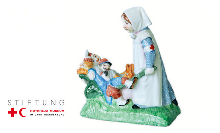 antike Porzellanfigur einer Rotkreuzschwester, die drei verwundete Soldaten in einer Karre vor sich herschiebt