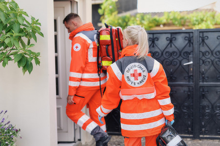 Ein Rettungssanitäter und eine Rettungssanitäterin des Roten Kreuz betreten ein Haus.