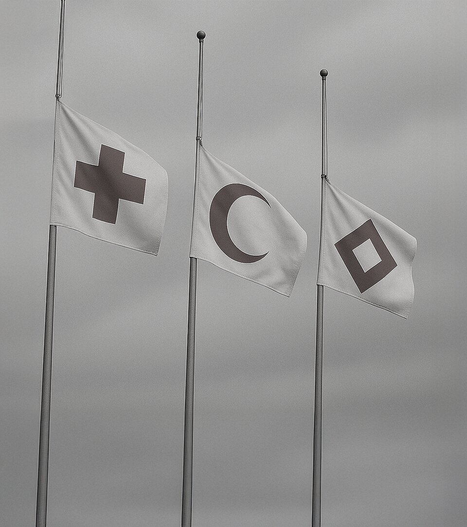 In schwarz-weiß hängen Flaggen des Roten Kreuzes, des Roten Halbmonds und des Roten Kristalls auf Halbmast (Bild: DRK).