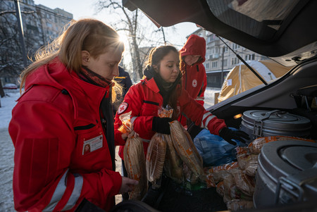 Drei Frauen in roten Einsatzjacken des Roten Kreuz geben in der Kälte warme Mahlzeiten aus.