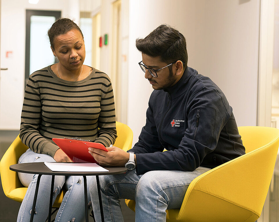 Ein Mitarbeiter des Roten Kreuz und eine Frau sitzen nebeneinander und sind im Gespräch.